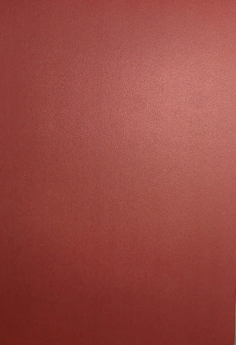 May include: A solid, flat sheet of paper or cardstock with a deep, muted red color. The surface has a subtle, fine-grained texture that is visible across the entire frame, creating a consistent, matte appearance without any patterns or designs.