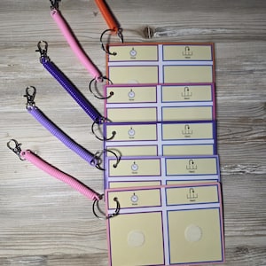 Puede incluir: Un conjunto de tarjetas de comunicaci&oacute;n coloridas con llaveros en espiral. Las tarjetas tienen un fondo amarillo claro con bordes morados y azules. Cada tarjeta tiene las palabras "Now" y "Next". Los llaveros son de color naranja, rosa y morado.