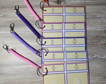 May include: A stack of colorful communication cards with spiral keychains. The cards have a light yellow background with purple and blue borders. Each card has the words "Now" and "Next" printed on them. The keychains are orange, pink, and purple.