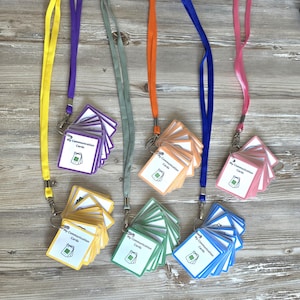 May include: A selection of communication cards on lanyards in a range of colours: yellow, purple, green, orange, blue, and pink. Each card features the text "My Communication Cards" and a small graphic on a white background. The cards are attached to the lanyards with metal clips.