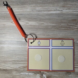 Puede incluir: Una tarjeta de programaci&oacute;n visual con un cord&oacute;n en espiral naranja y un clip met&aacute;lico. La tarjeta tiene un fondo amarillo claro con bordes morados y azules. La tarjeta est&aacute; etiquetada como "Ahora" y "Siguiente" con iconos correspondientes.