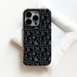 May include: Black phone case with a periodic table design. The case shows element symbols, atomic numbers, and atomic weights in white on a black background. The phone case is on a white surface.
