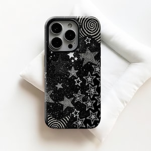 Może przedstawiać: Czarno-białe etui na telefon z motywem gwiazd i spiral. Etui ma czarne tło z białymi gwiazdami, spiralami i efektem brokatu. Etui ma czarną obwódkę i wycięcie na aparat.