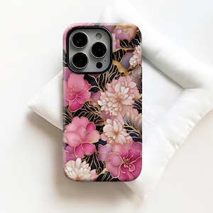 May include: A phone case with a floral pattern in shades of pink, white, and gold against a black backdrop. The case has a shiny finish and a camera aperture.