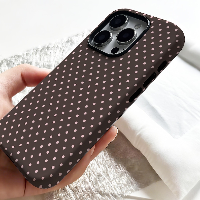 May include: A brown phone case with a repeating pattern of small, light pink polka dots. The case has a smooth surface and is designed to fit a smartphone, with cutouts for the camera and buttons.