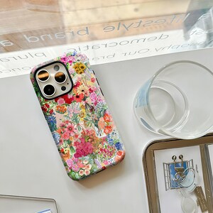May include: A floral patterned phone case featuring a vibrant mix of pink, red, yellow, and blue flowers. The case has a black border and covers the back and sides of the phone. The design includes various flower types and green foliage.