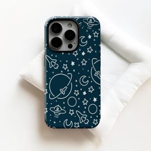 Puede incluir: Funda de teléfono azul oscuro con un diseño espacial blanco. El diseño incluye cohetes, planetas, estrellas, lunas y ovnis. La funda tiene un acabado brillante y un recorte para la cámara.