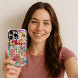 May include: A floral patterned phone case featuring a vibrant mix of red, pink, yellow, and blue flowers. The case has a white background and a glossy finish, offering a stylish and protective accessory for a smartphone.