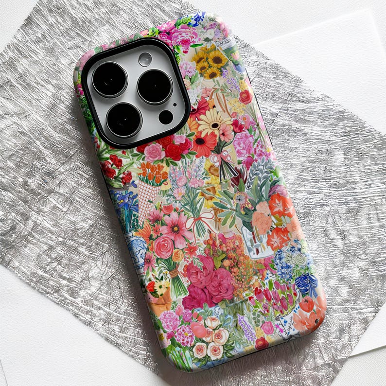 May include: A colorful phone case featuring a vibrant floral design. The case is covered in a collage of various flowers in shades of pink, red, yellow, and blue. The case has a camera cutout with three lenses.