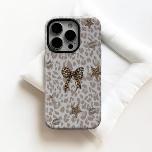 May include: A smartphone case with a light grey leopard print design. The case features a leopard print bow, star shapes, and lip prints. The case is designed to fit a smartphone.