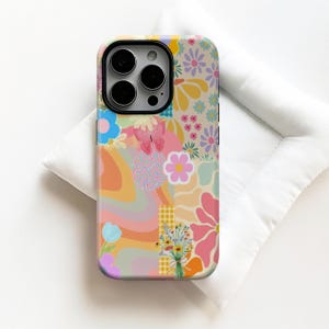 Puede incluir: Funda de teléfono colorida con un diseño de collage de patrones florales, una mariposa y formas abstractas en tonos rosa, naranja, azul y amarillo. La funda tiene un recorte negro para la cámara y un acabado brillante.