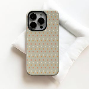 May include: A phone case with a repeating pattern of small, colorful polka dots in shades of orange, pink, and white on a light green background. The case has a black camera lens surround.