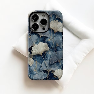 May include: A smartphone case featuring a blue and gold ginkgo leaf pattern. The case has a dark blue background with gold accents and a repeating pattern of stylized ginkgo leaves in shades of blue and silver. The case is resting on a white surface.