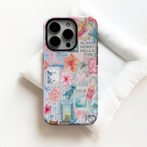 May include: A phone case with a collage design featuring tropical imagery. The case includes images of a seashell, hibiscus flowers, a flamingo, and the words "Aloha, Howdy, Hello" and "Coastal Life". The case is on a white surface.