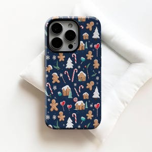 以下が含まれることがあります： ネイビーブルーの携帯電話ケース。ジンジャーブレッドマン、キャンディーケーン、ジンジャーブレッドハウス、雪の結晶、クリスマスツリーの繰り返し模様。光沢のある仕上がりです。
