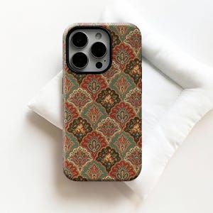 Op de afbeelding: Een telefoonhoesje met een herhalend patroon van bloemen en paisley-elementen in rood, groen en goud. De hoes heeft een zwarte cameramodule en ligt op een wit oppervlak.