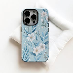May include: A smartphone case featuring a light blue background with a pattern of white flowers, blue leaves, and small white dots. The case has a black camera cutout area at the top left, showing three circular lenses and a flash component.