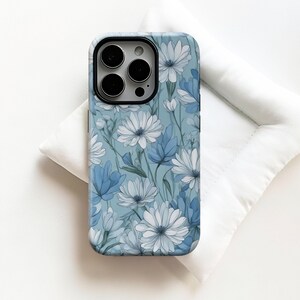 May include: A phone case with a floral design featuring white and blue flowers on a light blue background. The case has a black camera cutout and a glossy finish. The design includes detailed petals and leaves.