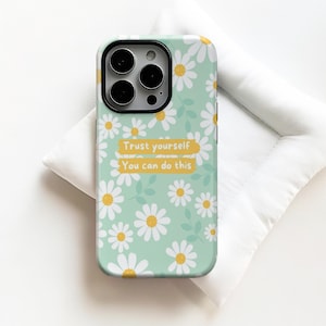 Puede incluir: Funda de teléfono con fondo verde claro, cubierta de margaritas blancas con centros amarillos y hojas verdes. La funda tiene el texto "Trust yourself, You can do this" en un rectángulo amarillo.