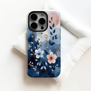 May include: A phone case with a floral design. It features blue, white, and pink flowers, and a pink sun. The case has a dark blue background with lighter blue cloud-like shapes. The phone case is on a white surface.