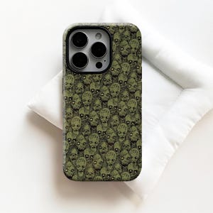 May include: A phone case with a repeating pattern of zombie faces in green and black. The case has a black camera lens cutout and a dark green border. The design is a detailed illustration of zombie faces.