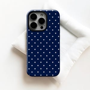 Puede incluir: Funda de teléfono azul marino con lunares blancos. La funda tiene un módulo de cámara negro y está sobre una superficie blanca. Diseñada para un smartphone.