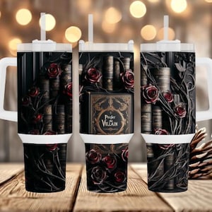 May include: A black tumbler featuring a design of antique books, red roses, and vines. The tumbler has a white handle and lid with a straw. The text "Prefer Villain" is visible on the front of the tumbler.
