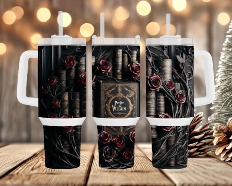 May include: A black tumbler featuring a design of antique books, red roses, and vines. The tumbler has a white handle and lid with a straw. The text "Prefer Villain" is visible on the front of the tumbler.