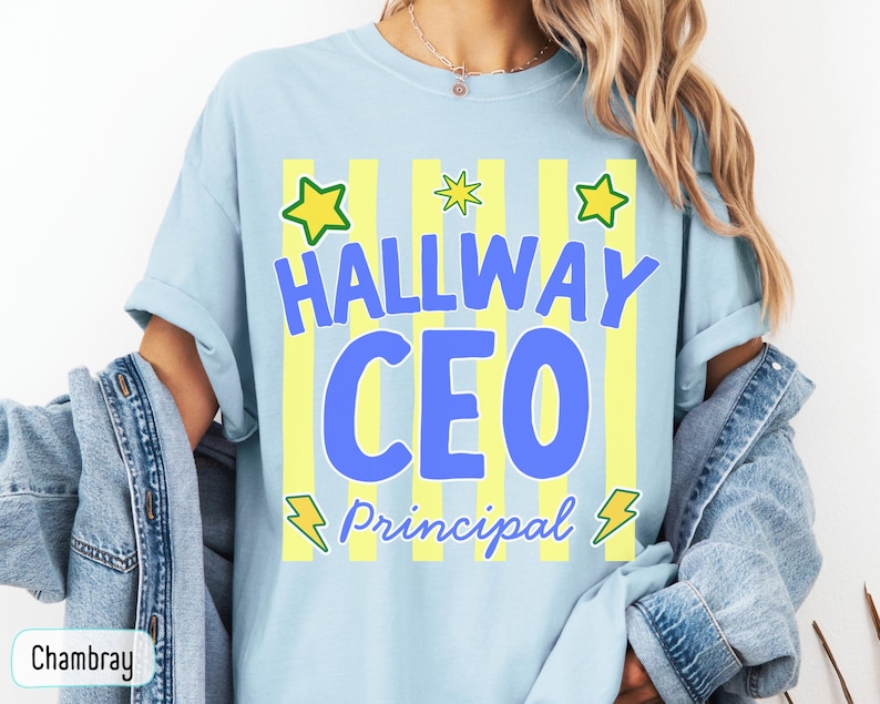 May include: A light blue t-shirt featuring a graphic with vertical yellow stripes, green stars, and yellow lightning bolts. The text reads "HALLWAY CEO" in large blue letters and "Principal" in smaller blue script font across the center.