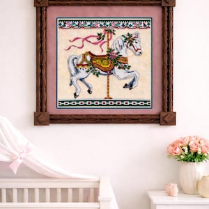 May include: A framed cross-stitch of a carousel horse. The white horse has a red bridle and saddle, adorned with green and pink floral accents. The artwork is framed in a dark brown wooden frame, with a pink and green border.