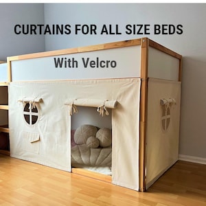 May include: Beige bed curtains with a tent-like design, featuring round windows and a pocket. The curtains are attached to a wooden frame and include the text "CURTAINS FOR ALL SIZE BEDS" and "With Velcro". Inside the tent are pillows.