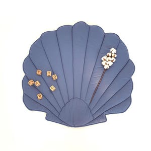 Könnte beinhalten: Eine blaue, muschelförmige Spielmatte mit Steppmuster. Holzbuchstabenwürfel sind auf der Matte verstreut. Ein Zweig Baumwolle setzt einen natürlichen Akzent. Die Matte ist für Babys und Kleinkinder konzipiert.