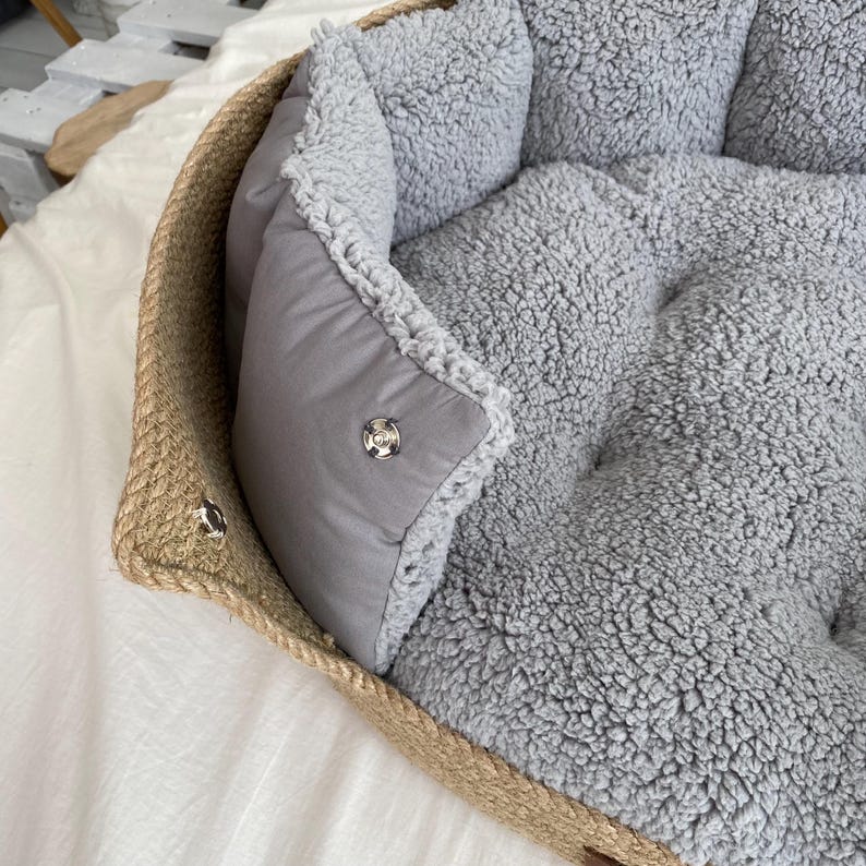 May include: A pet bed with a woven, rope-like border and a soft, gray, plush interior. The bed has a removable, gray, padded cushion with a snap closure. The bed is designed for small pets.