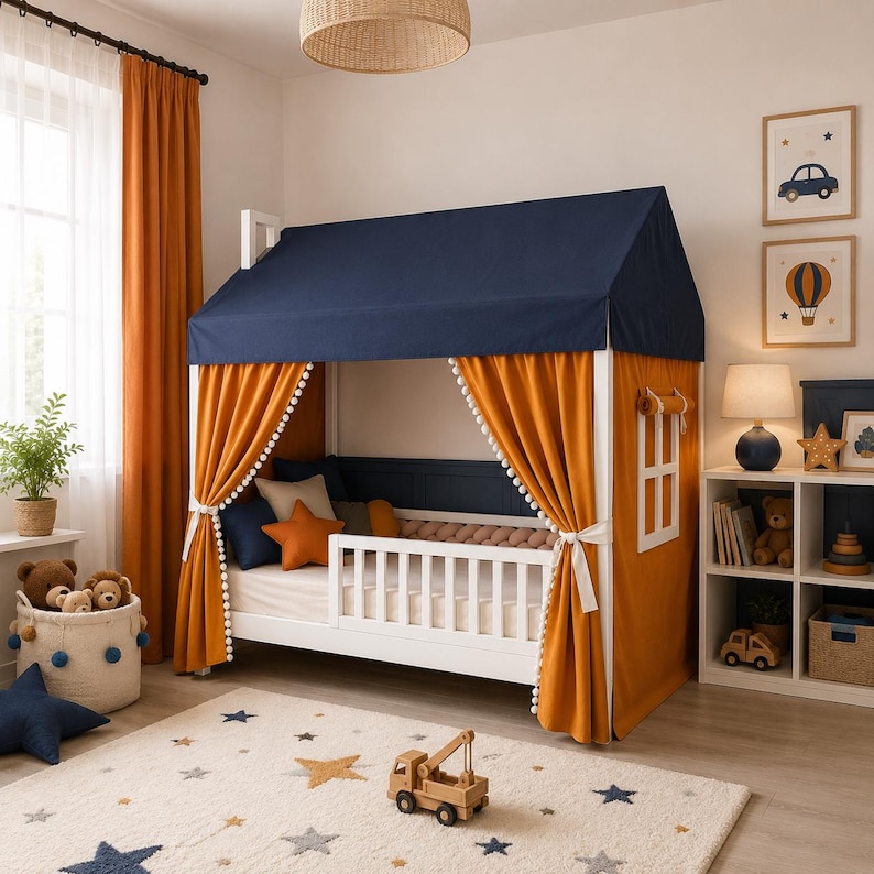 May include: A white house-shaped bed frame featuring a dark blue fabric roof and orange curtains with white pom-pom trim. The bed includes a white slatted safety rail, a mattress, and decorative pillows in orange and blue shades.