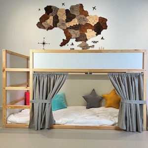 May include: A wooden bunk bed with a light-colored frame, featuring a lower bed with gray curtains and decorative pillows. A wooden map of Ukraine hangs on the wall above the bed, with airplane and compass decorations.