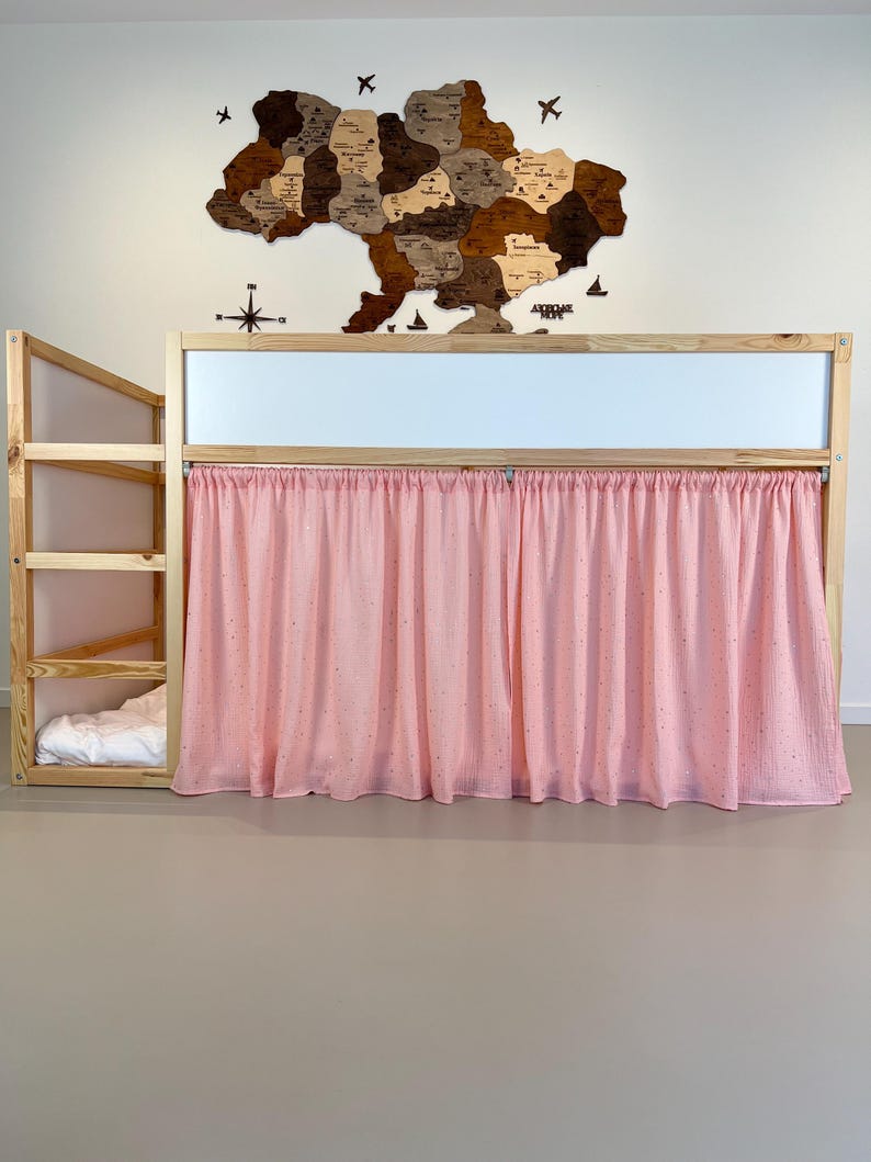 Pode incluir: Uma cama de beliche de madeira com uma cortina rosa claro. A cama tem uma escada e uma pequena &aacute;rea de cama. Um mapa de madeira da Ucr&acirc;nia est&aacute; montado na parede acima da cama.