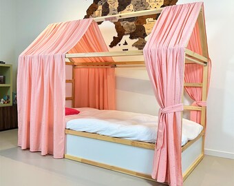 May include: A wooden house-shaped bed frame with pink curtains. The bed has a white mattress and a white and wood-colored base. A wooden world map is mounted on the wall above the bed.