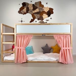Pode incluir: Uma cama de beliche de madeira com estrutura de madeira clara, cortinas rosa e almofadas em forma de estrela. Um mapa de madeira da Ucr&acirc;nia est&aacute; pendurado na parede acima da cama. A cama tem uma escada para acesso &agrave; cama superior.