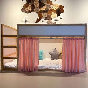 May include: A wooden bunk bed with a light-colored frame and pink curtains. The bed has a built-in ladder and shelves. A wooden map of Ukraine hangs on the wall above the bed, with a compass and airplane cutouts.