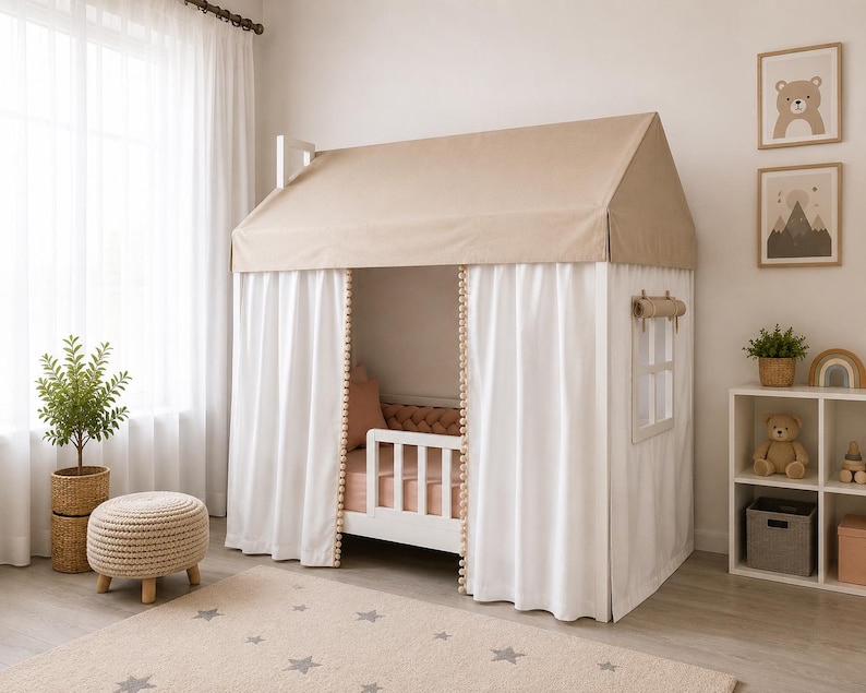 May include: A white house-shaped bed frame featuring a beige fabric roof, white curtains with pom-pom trim, and a side window with a roll-up shade. The bed includes a white safety rail and is dressed with a solid peach-colored mattress and pillow.