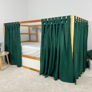 May include: A wooden bed frame with a white mattress and dark green curtains. The bed has a simple design with a natural wood finish. The curtains are hung from the top of the frame and drape down to the floor, creating a cozy space.