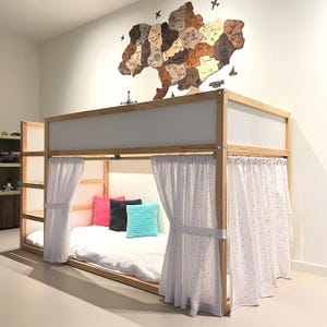 May include: A wooden bunk bed with white panels and curtains. The bed has a ladder and a lower bunk with a white mattress and colorful pillows. A wooden map of Ukraine hangs on the wall above the bed.