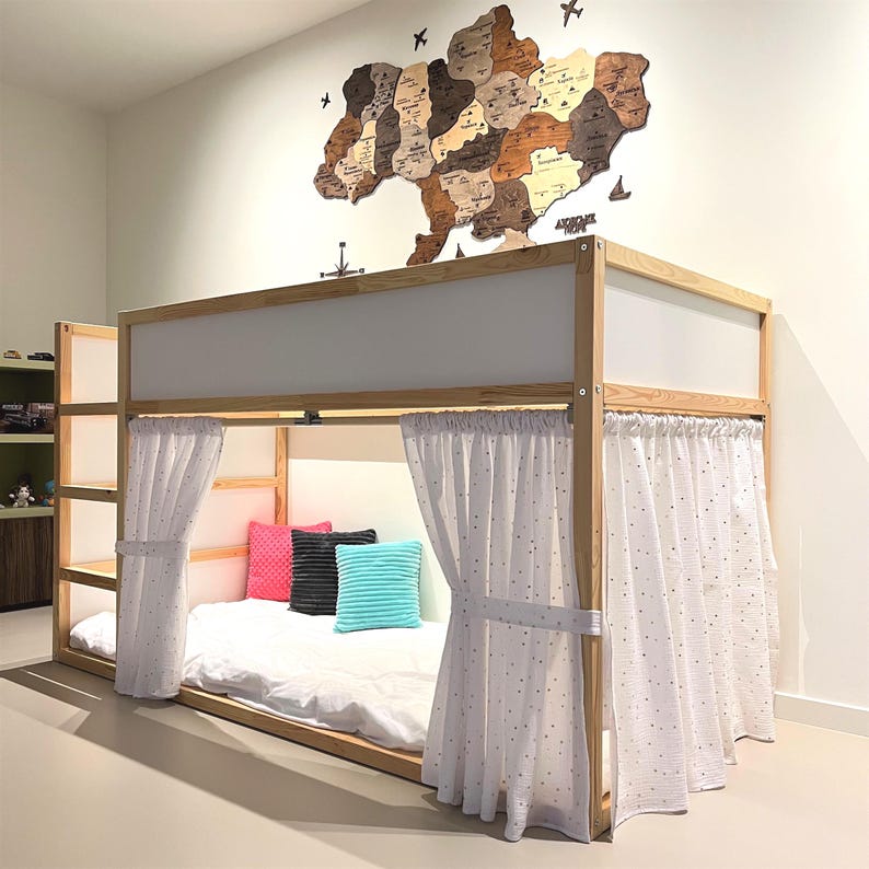 May include: A wooden bunk bed with white panels and curtains. The bed has a ladder and a lower bunk with a white mattress and colorful pillows. A wooden map of Ukraine hangs on the wall above the bed.