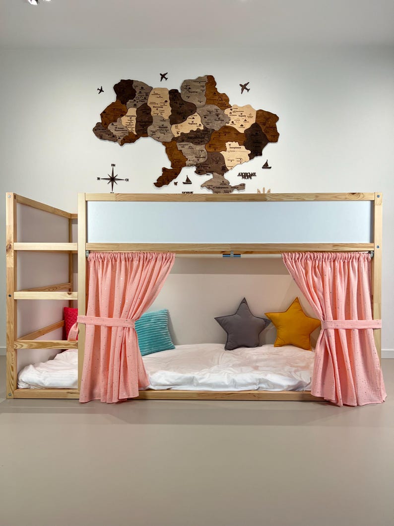 May include: A wooden bunk bed with a light wood frame, featuring a ladder and pink curtains. The bed is decorated with star-shaped pillows and a map of Ukraine on the wall. The bed has a white mattress.