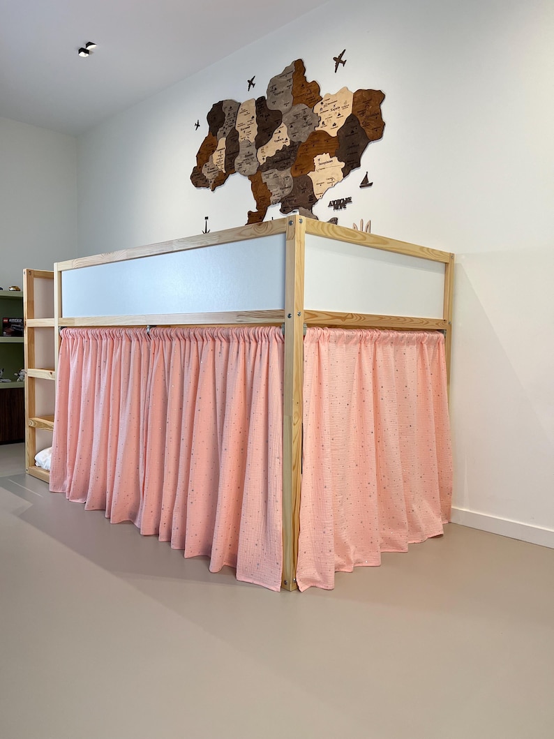 May include: A wooden bunk bed with a light pink curtain. The bed frame is made of light-colored wood. A wooden map of Ukraine hangs on the white wall above the bed.