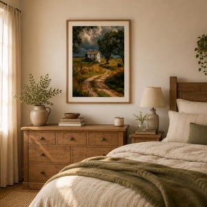 May include: A framed wall art print featuring a landscape painting of a white house at the end of a winding dirt path, surrounded by golden fields and dark, stormy clouds, displayed in a wooden frame on a light-colored wall above a dresser.