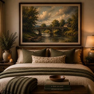 May include: A bedroom featuring a landscape painting of a stone bridge over a river above a bed with olive green pillows, a floral lumbar pillow, and a textured olive green throw blanket. A wooden bench holds a wooden bowl and three stacked books.
