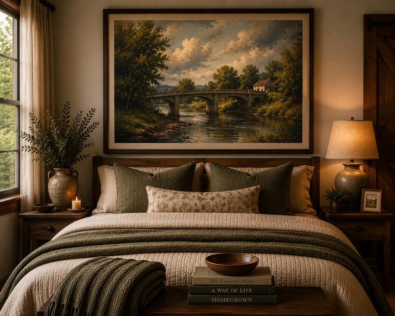 May include: A bedroom featuring a landscape painting of a stone bridge over a river above a bed with olive green pillows, a floral lumbar pillow, and a textured olive green throw blanket. A wooden bench holds a wooden bowl and three stacked books.