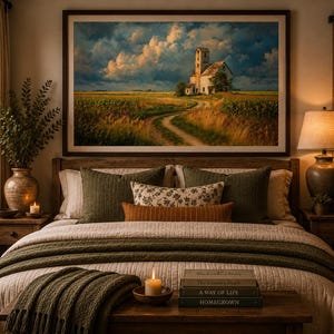 May include: A framed landscape wall art print depicting a rural scene with a stone building, a dirt path, and a field under a dramatic cloudy sky. The artwork is displayed above a bed with olive green pillows, a textured throw, and books.