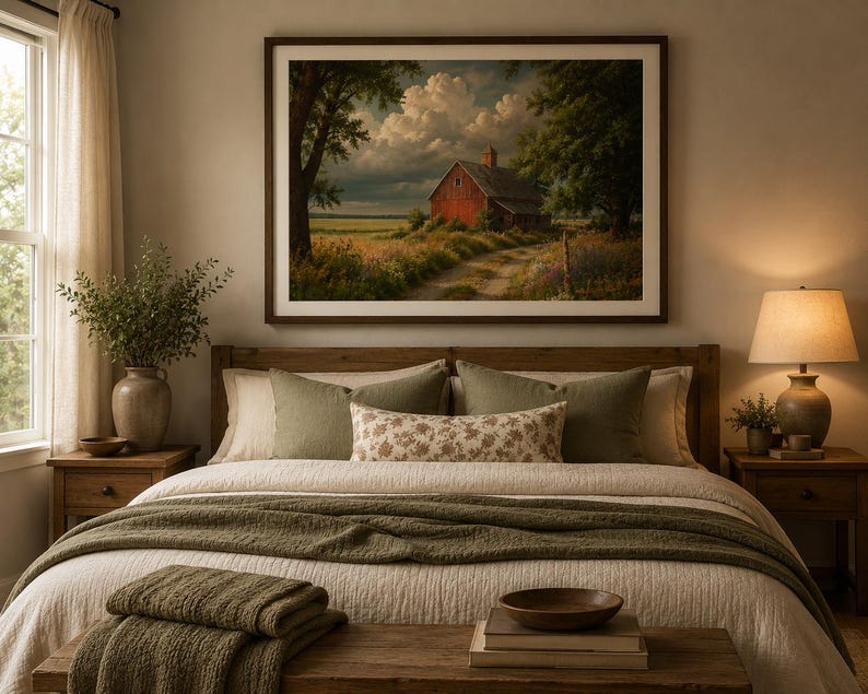 May include: A framed landscape wall art print featuring a red barn situated in a grassy field under a cloudy sky, displayed above a wooden bed frame with a white quilt, olive green throw blanket, and decorative pillows in a bedroom setting.